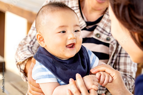 おばあちゃんに抱っこされた赤ちゃんがお母さんと戯れています　3世代が外のベンチに座っています