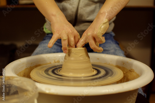 child potter's hands form by a clay pot on a potter's wheel. The potter works in a workshop