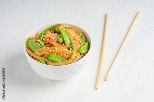Japchae savory vegetarian korean popular dish of stir-fried glass noodles and vegetables such as green peas, bean and carrot served in bowl with chopsticks on white wooden background for dinner
