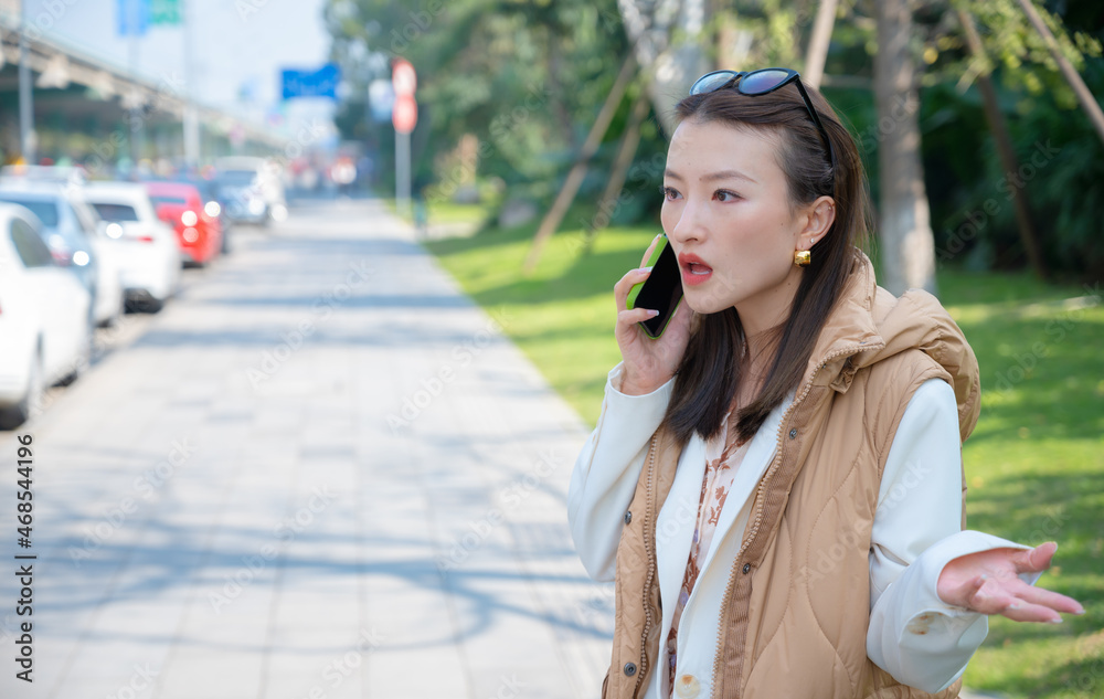 Portrait of pretty Chinese Asian young woman on street has mobile cell phone conversation holds near ear. Surprised misunderstanding emotions from call bad news mouth opened, warm clothes sunny day. Portrait of pretty Chinese Asian young woman on street has mobile cell phone conversation holds near ear. Surprised misunderstanding emotions from call bad news mouth opened, warm clothes sunny day.