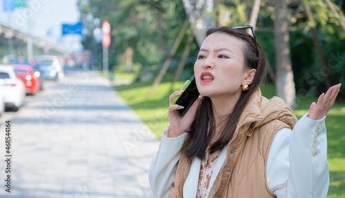 Portrait of pretty Chinese Asian young woman on street has mobile cell phone conversation holds near ear. Angry misunderstanding emotions from call bad news mouth opened, scammers calling shouting