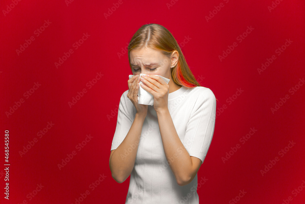 Running nose, flu symptoms. Sick girl sneezing blowing nose in napkin, suffering seasonal cold on red studio background Running nose, flu symptoms. Sick girl sneezing blowing nose in napkin, suffering seasonal cold on red studio background