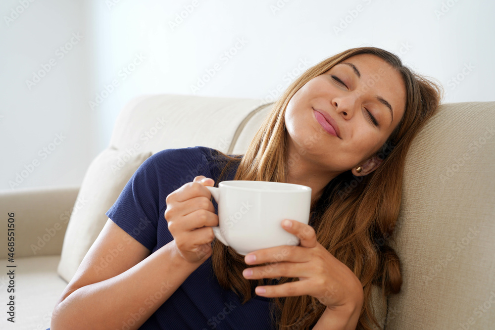 Dreamy smiling positive girl eyes closed holds cup with warm beverage imagining sitting on sofa Dreamy smiling positive girl eyes closed holds cup with warm beverage imagining sitting on sofa