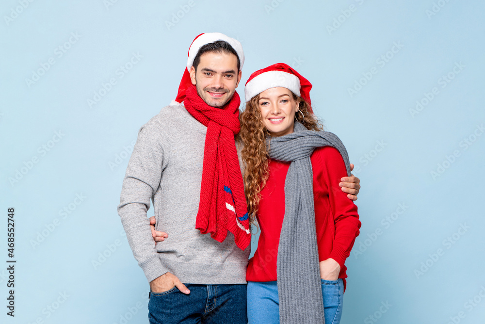 Portrait of happy Caucasian couple in Christmas outfits holding each other in light blue isolated studio background