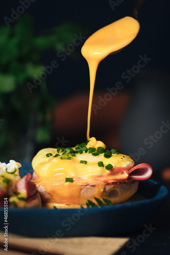 Tableau sur toile egg Benedict with hollandaise sauce on dark blue plate on table in kitchen
