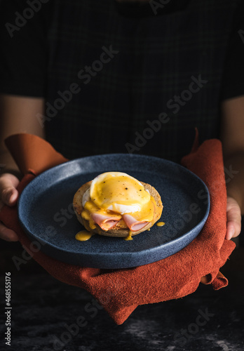 egg Benedict with hollandaise sauce on dark blue plate on table in kitchen photo