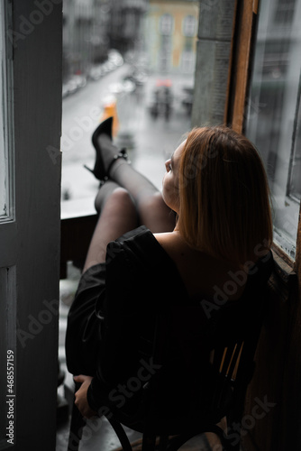 Beautiful young woman near the window on sunset. City view © alipko