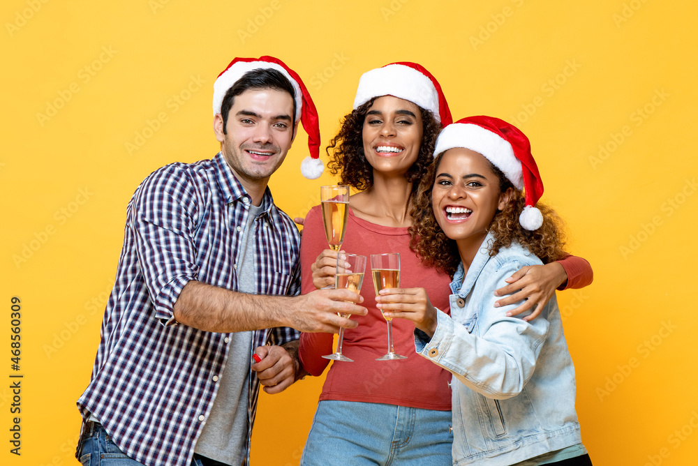 Fototapeta premium Group of three excited diverse friends celebrating Christmas drinking champagne together on yellow studio background
