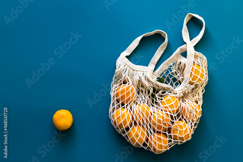 Mandarins or tangerines fruits in cotton eco-friendly mesh bag on blue background.