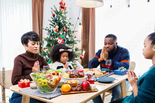 Families together to pray before meals at home. Celebration holiday togetherness near Christmas tree. African American family. Merry Christmas.