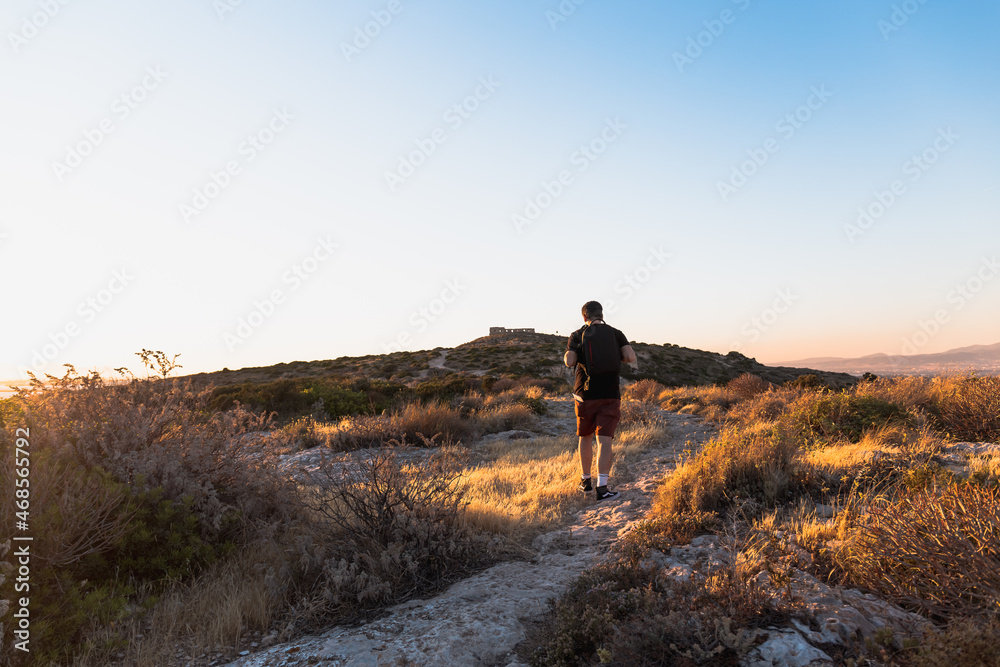 Panoramic back view of a backpacker trekking on the hills of Calamosca at sunset