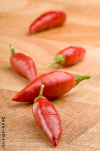 Five red chilli peppers arranged on a timber cutting board