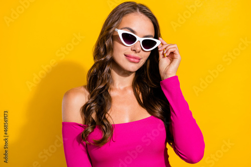 Portrait of attractive modern cheerful wavy-haired girl touching specs isolated over vibrant yellow color background