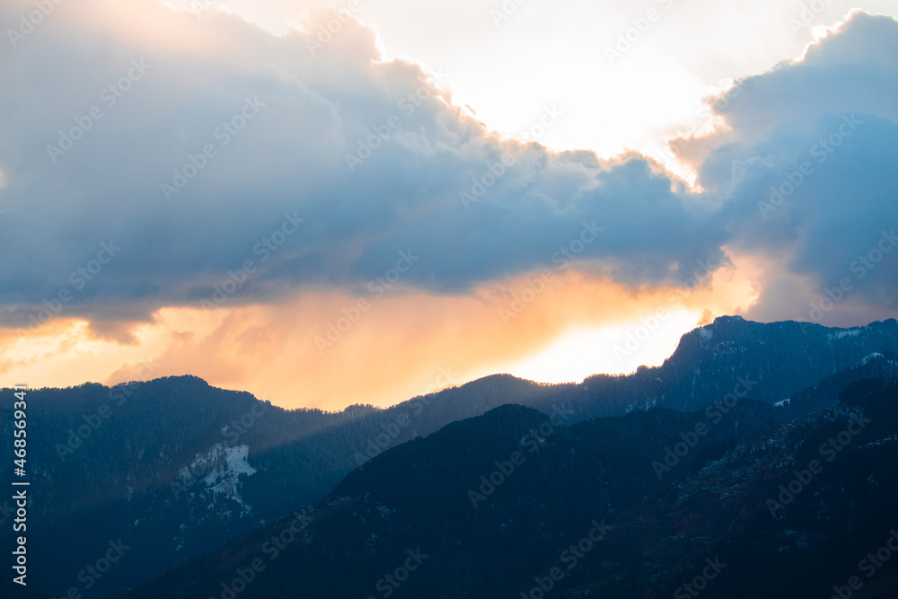 Orange clouds above the snow covered mountains of Kullu Valley during the sunset at Kullu in Himachal Pradesh, India. Beautiful sunset above the mountains besides Kullu in Himachal Pradesh, India.