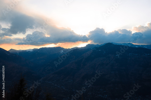 Orange clouds above the snow covered mountains of Kullu Valley during the sunset at Kullu in Himachal Pradesh  India. Beautiful sunset above the mountains besides Kullu in Himachal Pradesh  India.