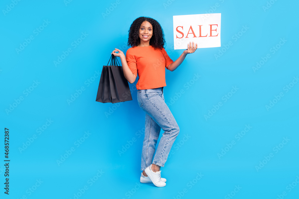 Full size photo of cheerful happy afro american nice woman hold sale banner bag isolated on blue color background Full size photo of cheerful happy afro american nice woman hold sale banner bag isolated on blue color background
