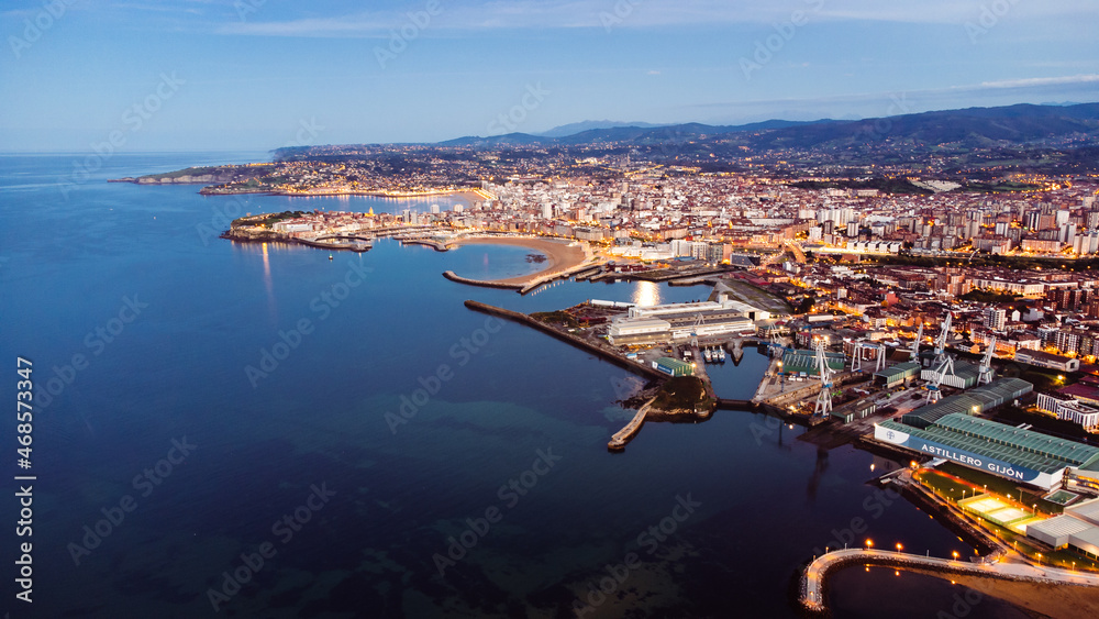 Drone above gijon city in Spain illuminated at night with city center traffic ocean seascape sand beach and harbor, aerial view of the main city in Galicia region