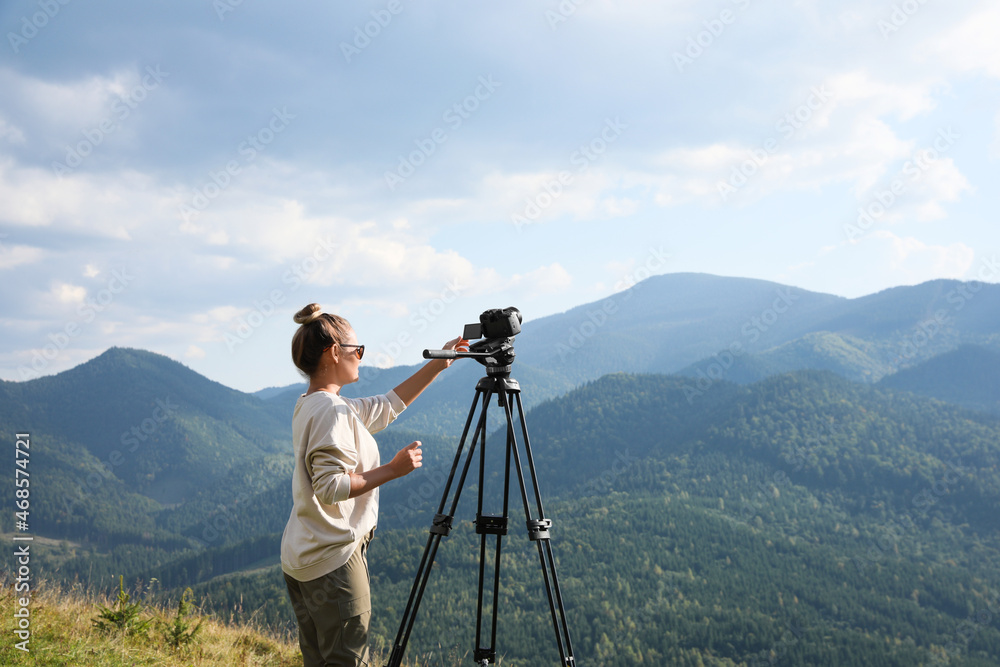 Professional photographer with modern camera on tripod in mountains. Space for text