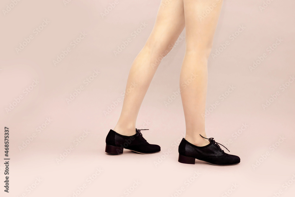 Black suede lace up shoes and woman's caucasian legs on light powdery pink background. English brogue Oxfords shoes. Studio shot photo. Copy apace.