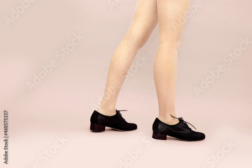 Fototapeta Naklejka Na Ścianę i Meble -  Black suede lace up shoes and woman's caucasian legs on light powdery pink background. English brogue Oxfords shoes. Studio shot photo. Copy apace.