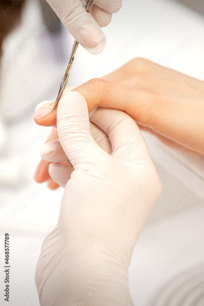 Close up of manicure master with manicure scissors removes cuticles on female nails at a beauty salon Close up of manicure master with manicure scissors removes cuticles on female nails at a beauty salon