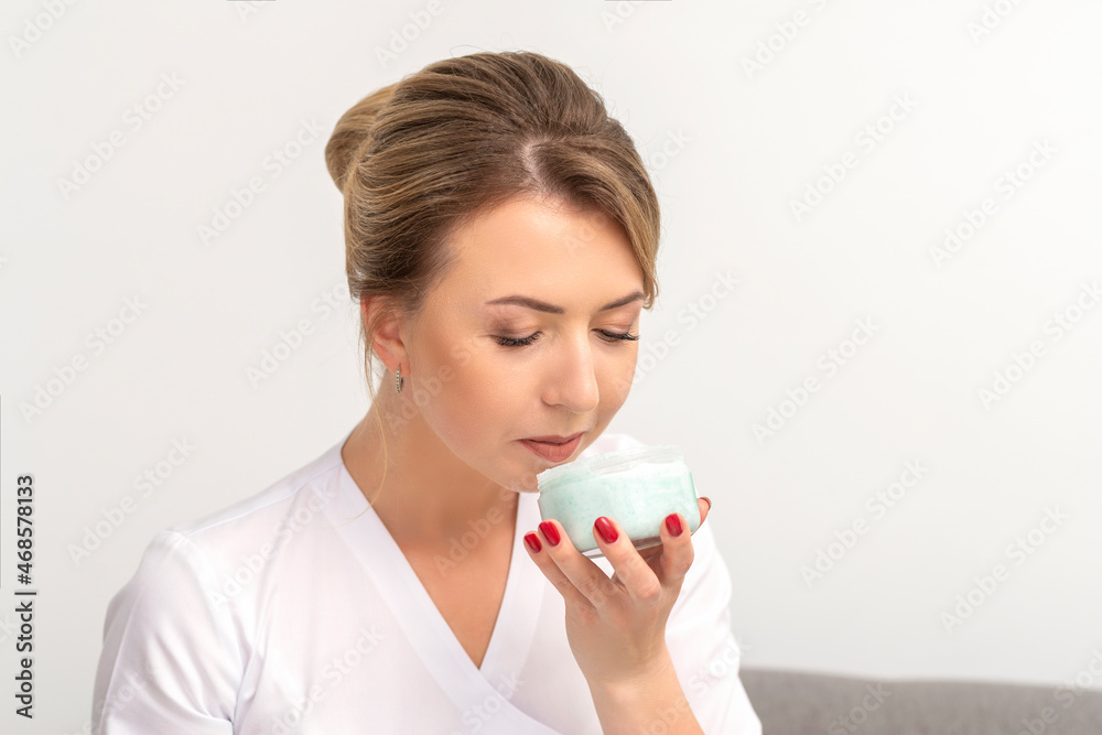 Portrait of young beautician sniffing moisturizing cream holding white jar on white background, copy space Portrait of young beautician sniffing moisturizing cream holding white jar on white background, copy space