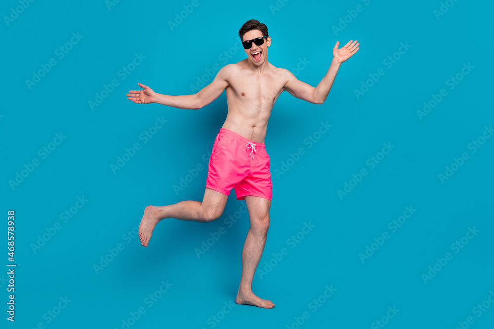 Photo of positive funny young guy topless dark eyewear smiling dancing isolated blue color background