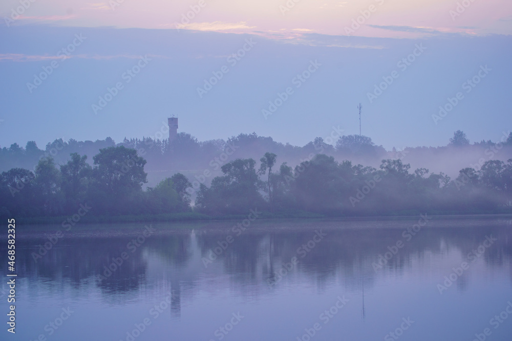 misty morning by the lake with calm water, fog and reflections of trees in mirror