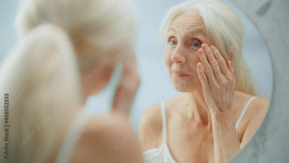 Portrait of Beautiful Senior Woman Morning Routine, Looking into Mirror Gently Applying Face Cream. Elderly Lady Makes Her Skin Soft, Smooth, Wrinkle Free with Natural anti-aging Cosmetics, Products Portrait of Beautiful Senior Woman Morning Routine, Looking into Mirror Gently Applying Face Cream. Elderly Lady Makes Her Skin Soft, Smooth, Wrinkle Free with Natural anti-aging Cosmetics, Products