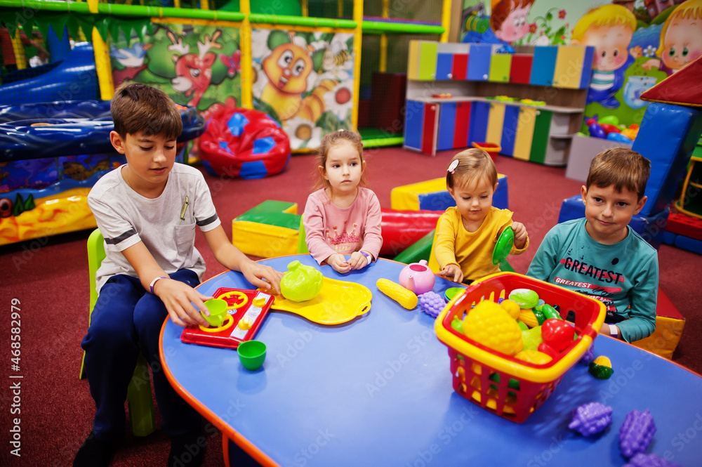 Fototapeta premium Four kids playing in indoor play center. Kindergarten or preschool play room. Sitting by the table with plastic fruits.