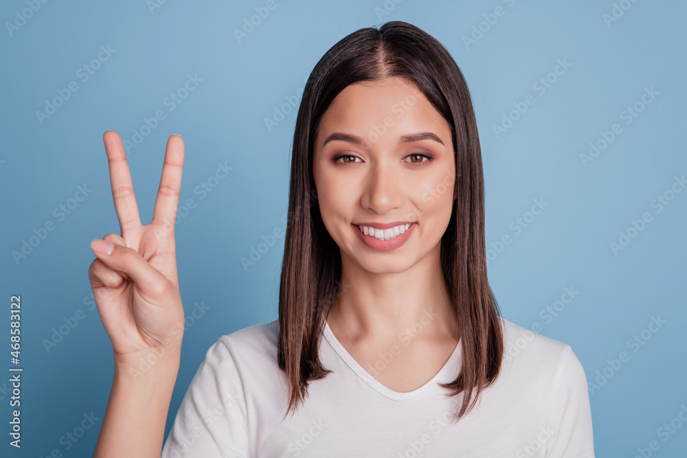 Photo of friendly pretty gorgeous girl show v-sign peace gesture on blue background Photo of friendly pretty gorgeous girl show v-sign peace gesture on blue background