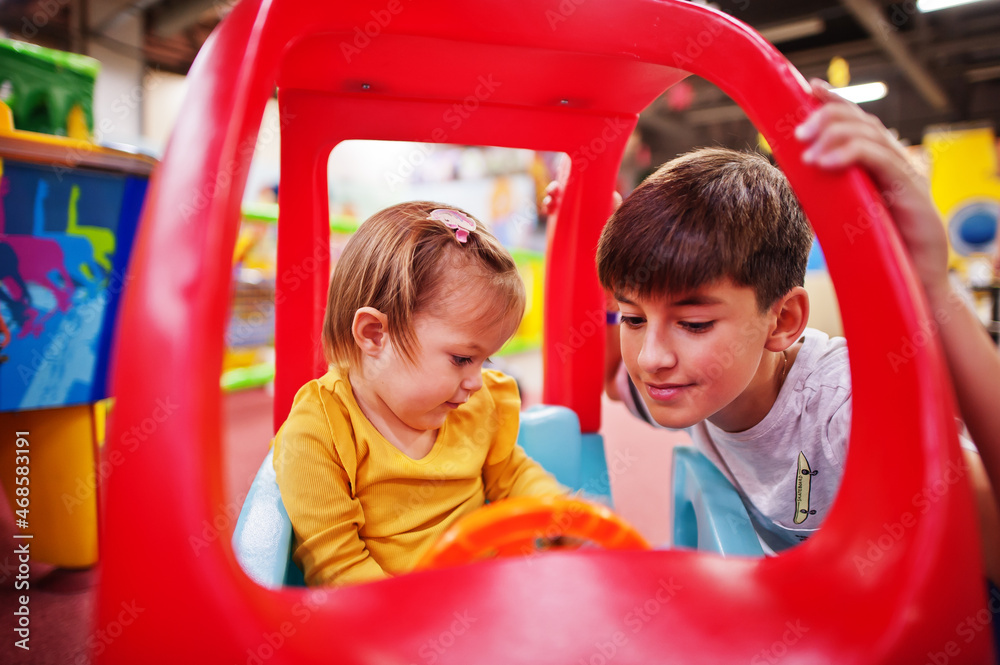 Brother with sister rides on a plastic car in indoor play center. Brother with sister rides on a plastic car in indoor play center.