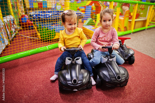 Two siters rides on a plastic cars in indoor play center.