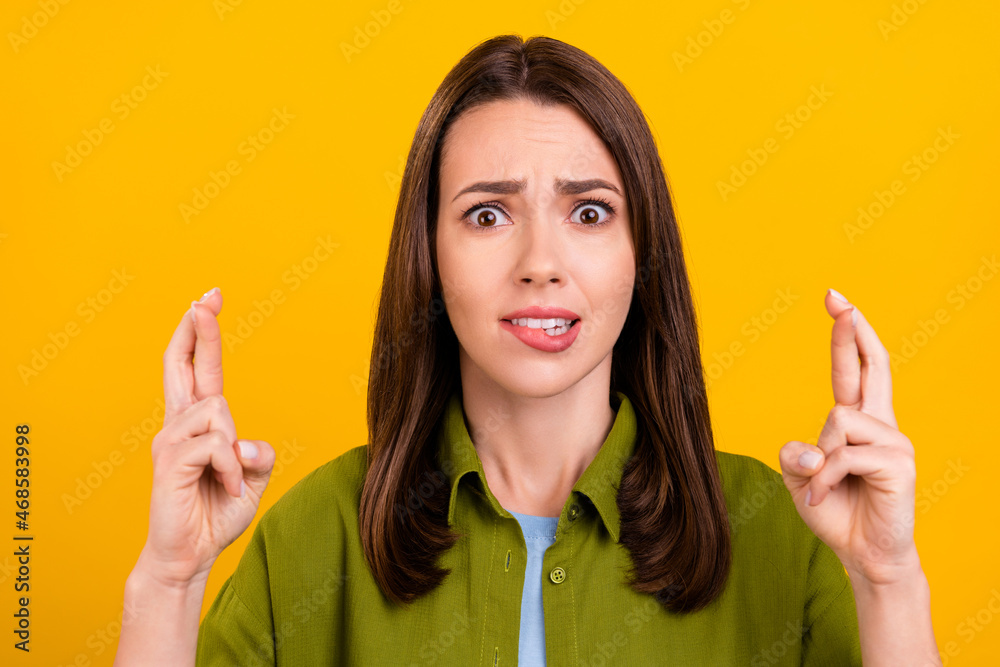 Photo of unsure unhappy young woman dressed green shirt biting lip fingers crossed isolated yellow color background Photo of unsure unhappy young woman dressed green shirt biting lip fingers crossed isolated yellow color background