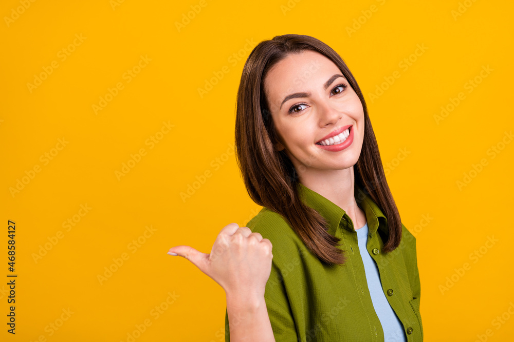 Photo of excited sweet young woman dressed green shirt smiling pointing back finger empty space isolated yellow color background Photo of excited sweet young woman dressed green shirt smiling pointing back finger empty space isolated yellow color background