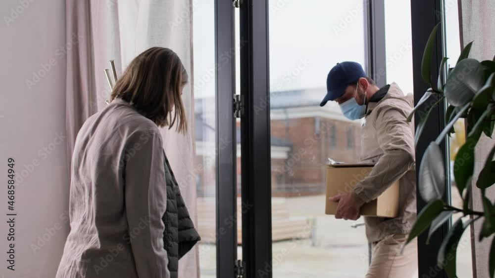 health protection, safety and pandemic concept - delivery man in face protective mask with parcel box and female customer signing papers at home health protection, safety and pandemic concept - delivery man in face protective mask with parcel box and female customer signing papers at home