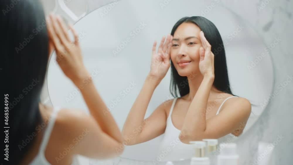 Beautiful Asian Woman Plays and Admires Her Perfect Soft Skin and Lush Black Hair, Looks at Camera and Smiles in the Bathroom Mirror. Concept for Wellbeing, Natural Beauty, Organic Skincare Products Beautiful Asian Woman Plays and Admires Her Perfect Soft Skin and Lush Black Hair, Looks at Camera and Smiles in the Bathroom Mirror. Concept for Wellbeing, Natural Beauty, Organic Skincare Products