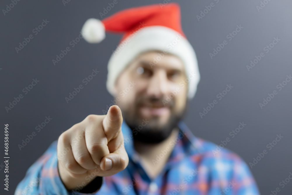 The hand of a man in a plaid shirt and a Santa hat points forward with his index finger. Focus on the hand. The hand of a man in a plaid shirt and a Santa hat points forward with his index finger. Focus on the hand.