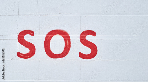Image of the universal relief word sos painted in red on a white wall. help and assistance concept