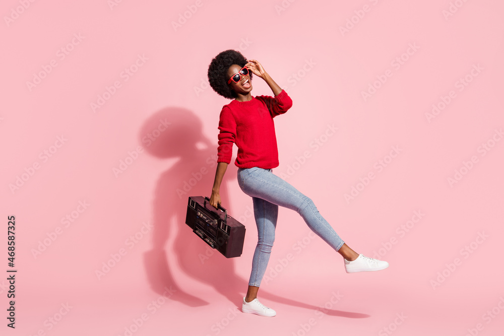 Full size profile portrait of carefree excited dark skin girl hold boombox touch sunglass isolated on pink color background