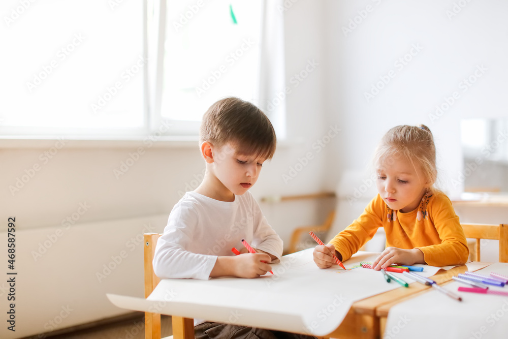 Funny kids Toddlers draw together with felt-tip pens on paper at the table, Montessori and creativity, creative development and activities in kindergarten. Boy and girl painting together Funny kids Toddlers draw together with felt-tip pens on paper at the table, Montessori and creativity, creative development and activities in kindergarten. Boy and girl painting together