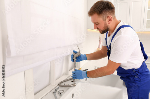 Professional plumber repairing water tap in kitchen