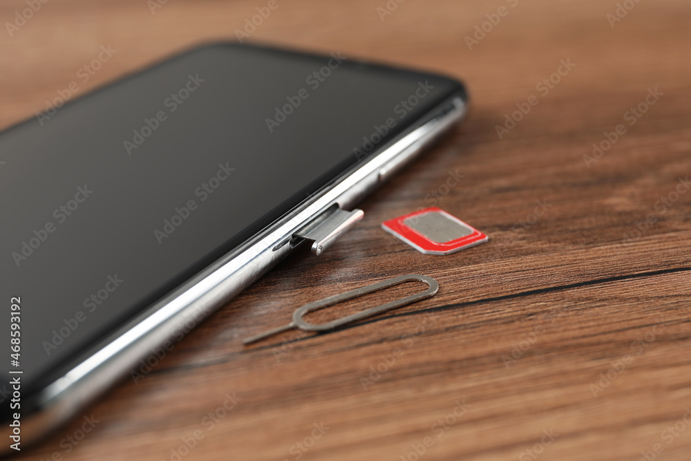 Mobile phone, SIM card and ejector tool on wooden table, closeup Mobile phone, SIM card and ejector tool on wooden table, closeup