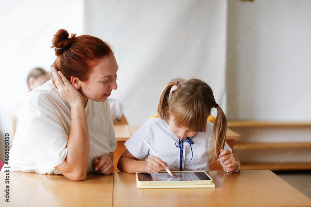 teacher and girl student child at school at desk works with digital tablet, gadgets in classroom and in education, modern education and technology, teacher and student learning with digital tablet teacher and girl student child at school at desk works with digital tablet, gadgets in classroom and in education, modern education and technology, teacher and student learning with digital tablet