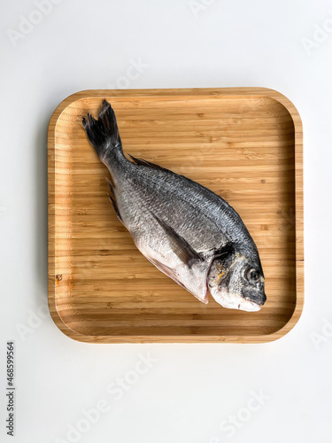 Raw dorado fish on the wooden plate on white background. Top view. Cooking fish. photo