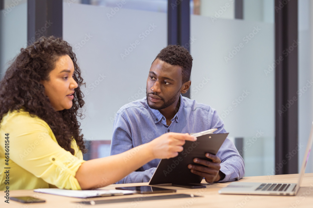 Two diverse business people sitting at table and discussing in modern office Two diverse business people sitting at table and discussing in modern office