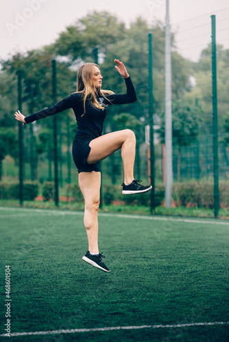 Young female in sportswear lunges and jumps on sports ground. Side view.