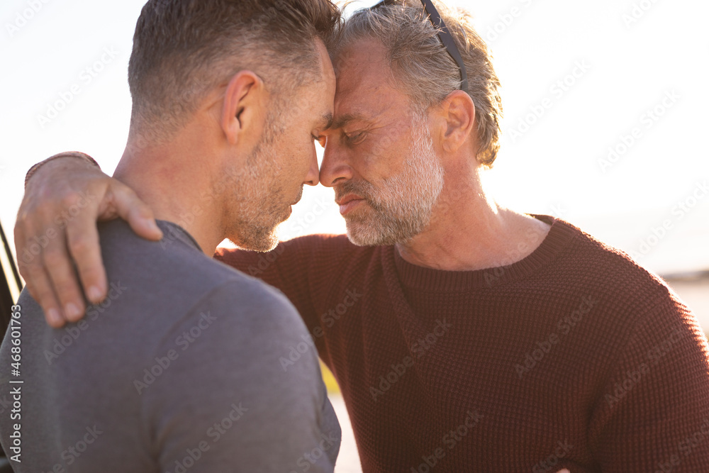 Happy caucasian gay male couple embracing in sun at seaside Happy caucasian gay male couple embracing in sun at seaside