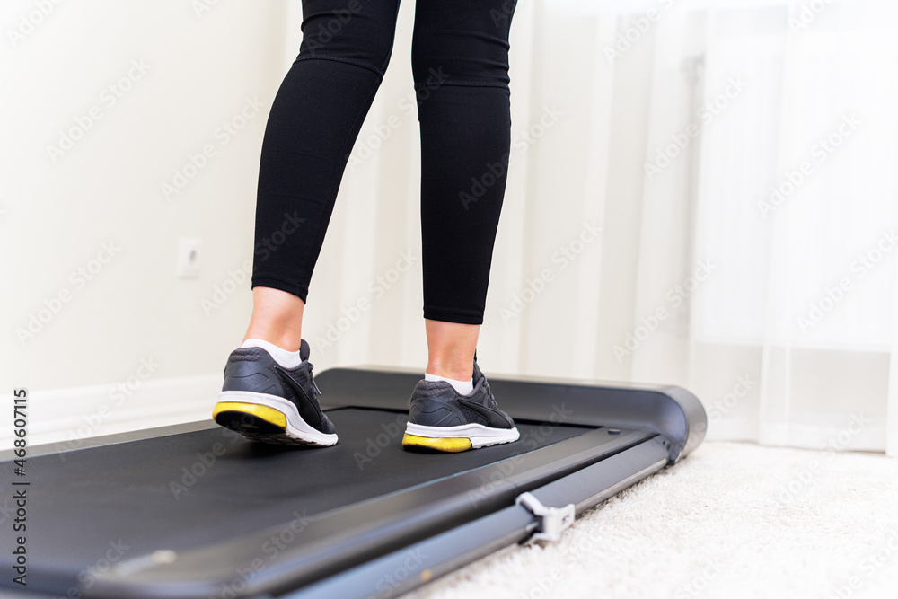 Sporty woman using walking treadmill in the interior of the room or home.