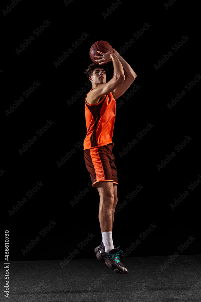 Full length portrait of basketball player training isolated on dark studio background. Tall muscular athlete jumping with ball. Full length portrait of basketball player training isolated on dark studio background. Tall muscular athlete jumping with ball.